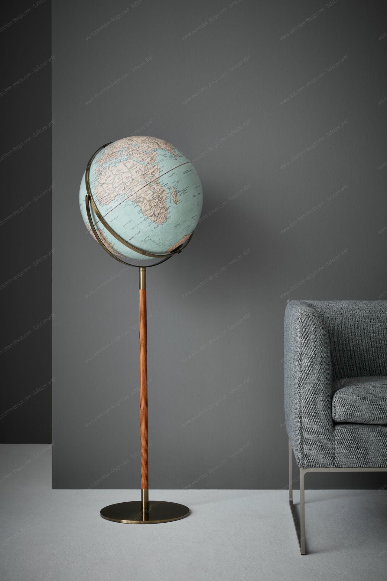 Standglobus des Herstellers Emform mit elegantem Holzgestell auf einem Metall Tellerfuß. Der Globus steht vor einer grauen Wand und neben einem Sofa.